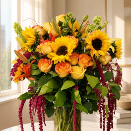 Bouquet of yellow sunflowers and orange-tipped roses in a clear glass vase