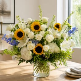 Large bouquet of white roses, sunflowers, and blue flowers in a glass vase
