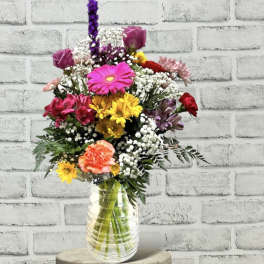 Mixed bouquet in a clear glass vase with pink, yellow, purple, and white flowers