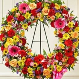 Large bright multicolored standing wreath of mixed flowers with a pink ribbon on an easel