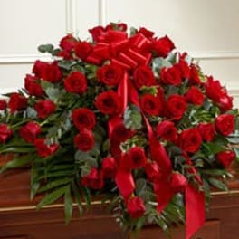 Red rose casket spray with a large red ribbon on a wooden casket