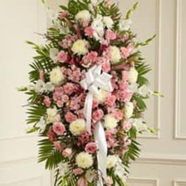 Tall standing spray of pink roses and carnations with white mums and a white bow on an easel