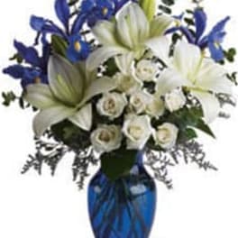 Tall arrangement of white lilies and roses with blue irises in a cobalt glass vase