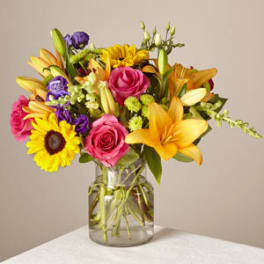 Mixed bouquet of roses, lilies, and sunflowers in a glass vase
