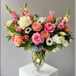 Mixed pink and peach flowers arranged in a clear glass vase