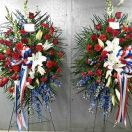 Two large standing floral sprays with red roses, white lilies, and blue accents
