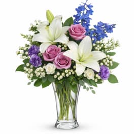 Bouquet of white lilies, pink roses, and blue flowers in a clear glass vase