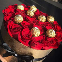 Red roses arranged in a round gold box with gold-wrapped chocolates on top