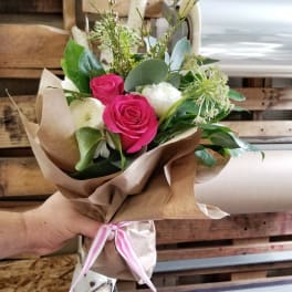 Hand-tied bouquet of pink and white roses wrapped in brown paper