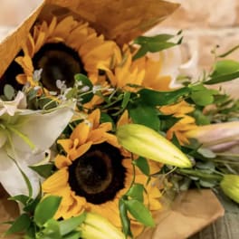 Bouquet with sunflowers, white lilies, and unopened lily buds in brown paper