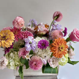 Mixed bouquet of pink, orange, and lavender flowers in a wooden box