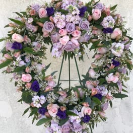 Heart-shaped floral wreath with pink and lavender roses on a stand
