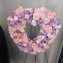 Heart-shaped floral wreath in pink, lavender, and white on a stand