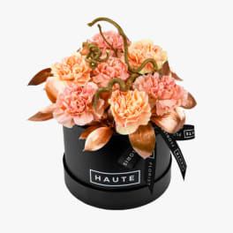 Peach carnations arranged in a black round box with ribbon