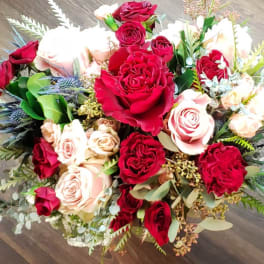 Bouquet of red and blush roses with mixed greenery on a wooden floor