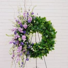 Large floral wreath with purple blooms and dense green foliage on a stand