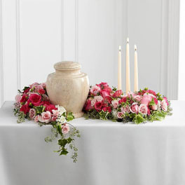 Pink and red rose arrangements around a beige urn with three taper candles