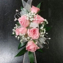Pink rose corsage with baby's breath and silver ribbon on a dark background