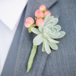 Succulent boutonniere with pink berries pinned to a gray suit lapel