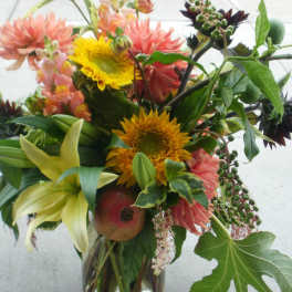 Loose garden-style bouquet with yellow sunflowers, peach dahlias, and lilies in a clear glass vase