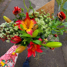 Handheld bouquet of red and orange lilies with small white filler flowers in kraft paper wrap