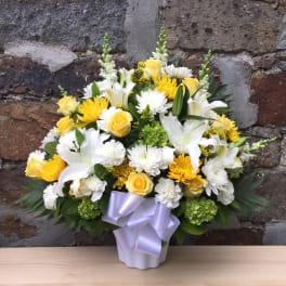 Yellow and white floral arrangement in a lavender vase with a ribbon bow