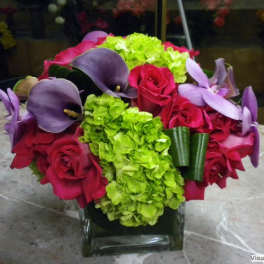 Bouquet of red roses, purple calla lilies, and green hydrangeas in a glass vase