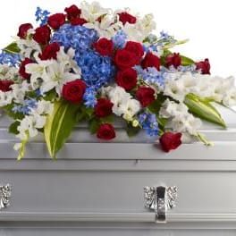 Red roses, white lilies, and blue flowers arranged on a white casket