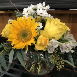 Yellow roses and a sunflower in a glass vase with white daisies