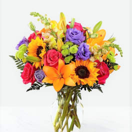 Bright mixed bouquet of roses, lilies, and sunflowers in a clear glass vase