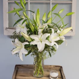 White lilies arranged in a clear glass vase with a small candle nearby.