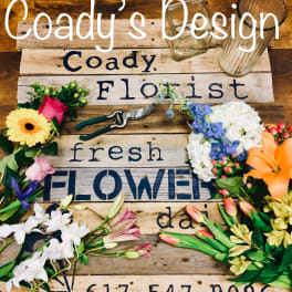 Assorted flowers arranged around a wooden sign with glass vases