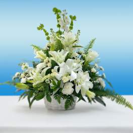 White lilies and roses arranged in a basket with a white ribbon
