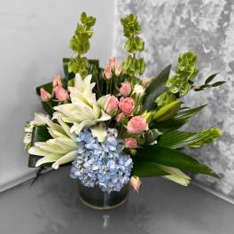 White lilies, pink roses, and blue hydrangea in a dark vase