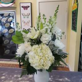 White floral arrangement in a white vase with lilies, hydrangea, and chrysanthemums