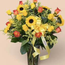 Sunflowers and orange-yellow roses in a clear glass vase with a yellow ribbon