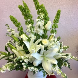 White lilies and roses in a white vase with tall green spikes