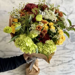 Mixed bouquet of yellow, lime green, and burgundy flowers wrapped in paper