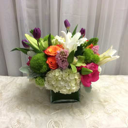 Mixed bouquet with lilies, tulips, roses, and hydrangea in a square vase