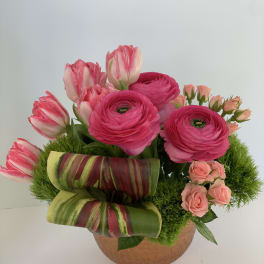 Pink tulips and ranunculus in a round vase with striped leaves