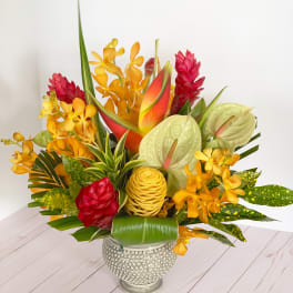 Tropical flower arrangement in a textured silver vase with red, orange, and green blooms