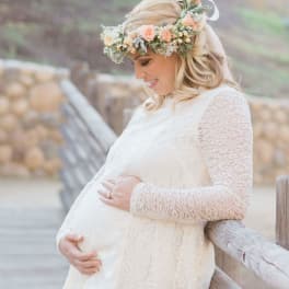 Pregnant woman in a white lace dress wearing a pastel flower crown