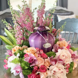 Pink and peach floral arrangement around a purple urn on a table