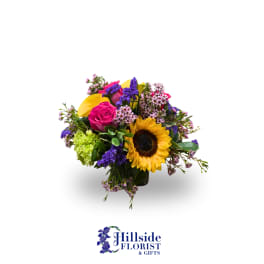 Colorful mixed bouquet with sunflower, pink rose, and purple accents in a glass vase