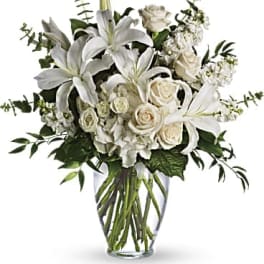 Arrangement of white lilies, roses, and hydrangeas in a clear glass vase