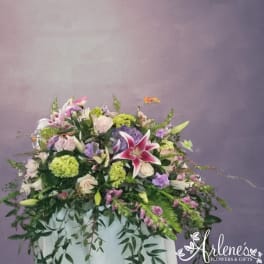 Large floral arrangement with pink lilies, roses, and purple blooms in a white container