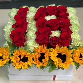 Red roses and white roses arranged in a white box with sunflowers along the front