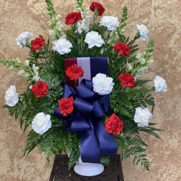 Red and white carnations in a white vase with a large blue ribbon