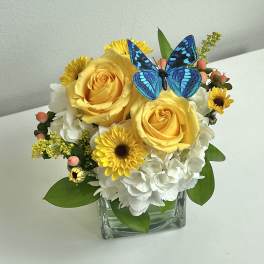 Yellow roses and white hydrangeas in a glass vase with a blue butterfly accent