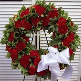 Red floral wreath with a white ribbon bow on a stand